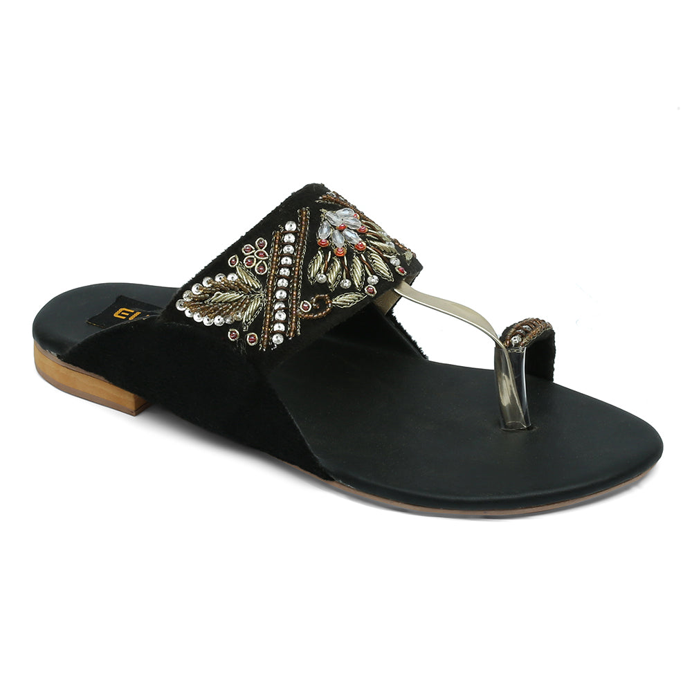A black sandal with detailed handmade embellishments and a strappy design with floral patterns and red stones.