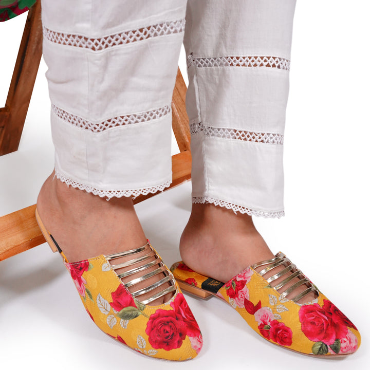 Yellow floral slippers with red roses worn by a person sitting on a wooden chair.