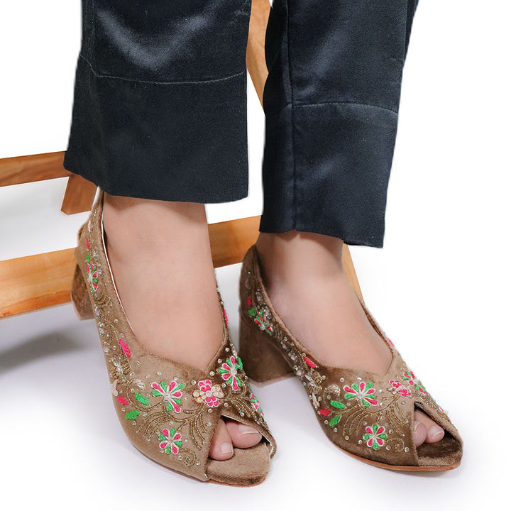 Brown open-toe shoes with floral embroidery worn by a person sitting on a chair.
