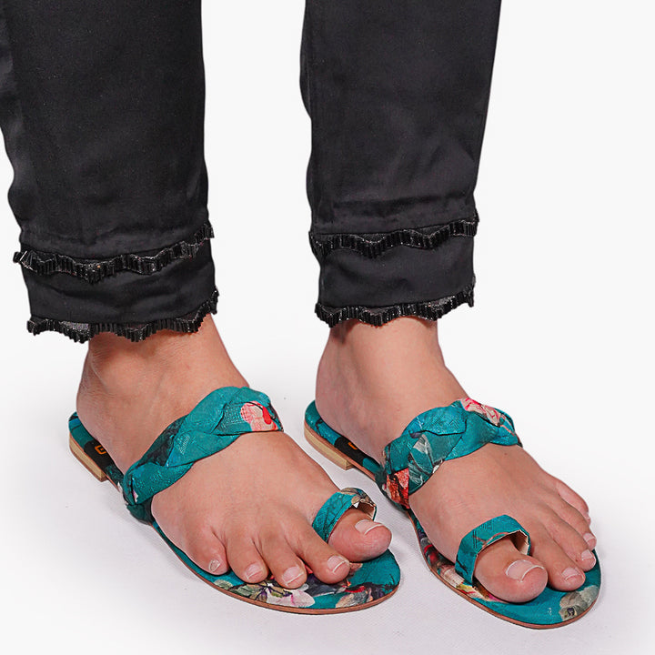 Teal sandals with floral pattern worn by a person on a white background