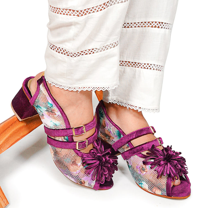 Purple floral sandals worn with white pants on a white background