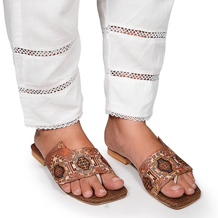 Brown embroidered sandals worn with white pants on a white background