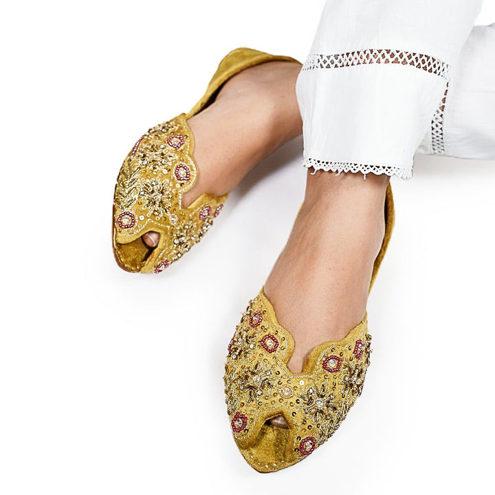 Yellow embellished shoes worn by a person on a white background