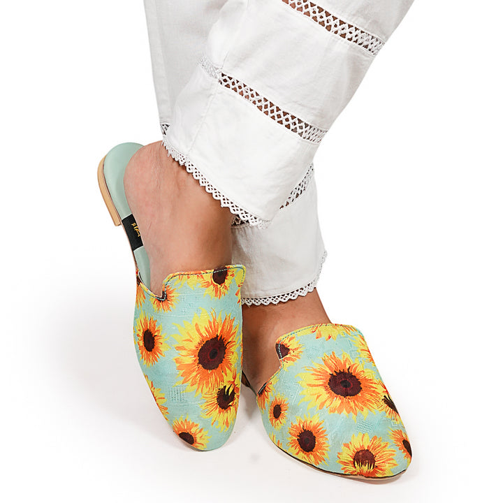 Sunflower-patterned slippers worn with white pants on a light background
