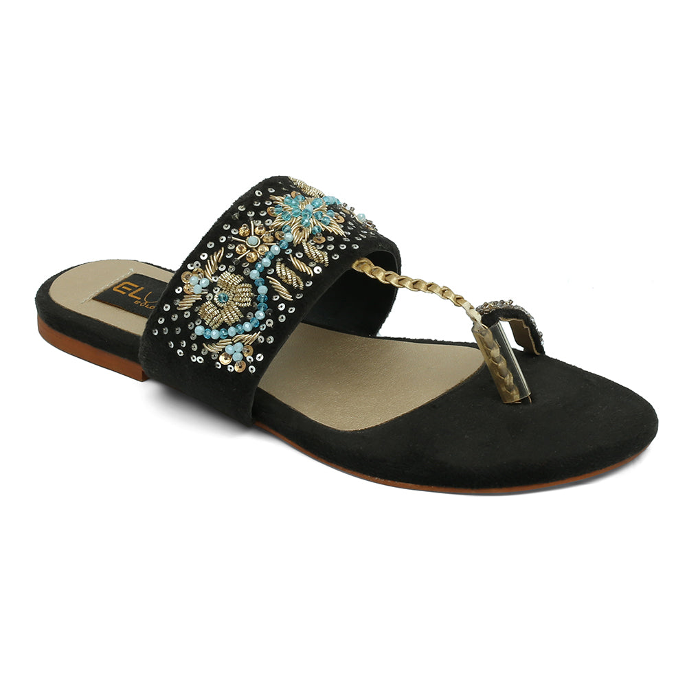 A black sandal with intricate handmade embellishments and a brown leather sole.